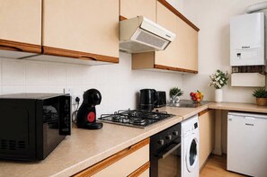 A modern kitchen with a microwave, coffee maker, gas stove, washing machine, and a dishwasher. - Stylish 1BR in Vibrant Fitzrovia, Steps from Soho (London)