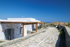 A white building with a stone pathway, wooden pergola, and a view of the landscape.