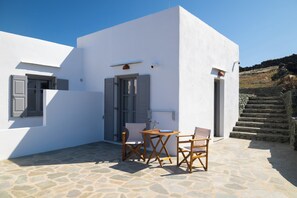Un edifici blanc amb sòl de pedra, una taula amb caires i una porta.