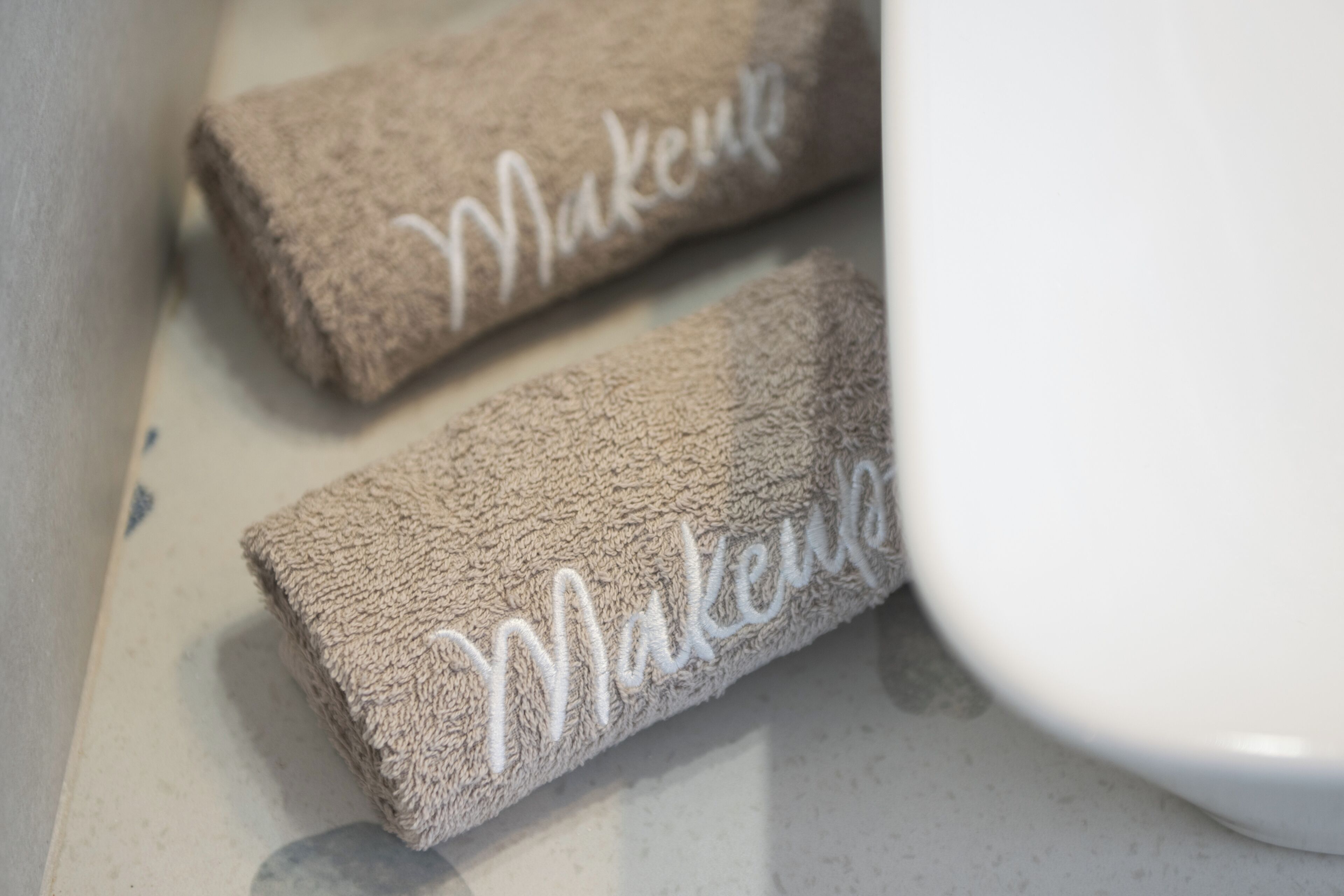 Två handdukar med ordet ”Makeup” broderat på dem, placerade på en vit yta.
