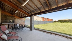 An outdoor patio with a table and chairs, a stone wall, and a view of a grassy yard and buildings. - 4-bedroom family home with a garden and easy parking, just outside Toulouse (Aucamville)
