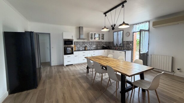 A modern kitchen with a dining area, featuring a wooden table, white chairs, and pendant lighting. - 4-bedroom family home with a garden and easy parking, just outside Toulouse (Aucamville)