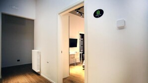 A hallway with a radiator, a door leading to a room with a desk and chair, and a sign on the wall.