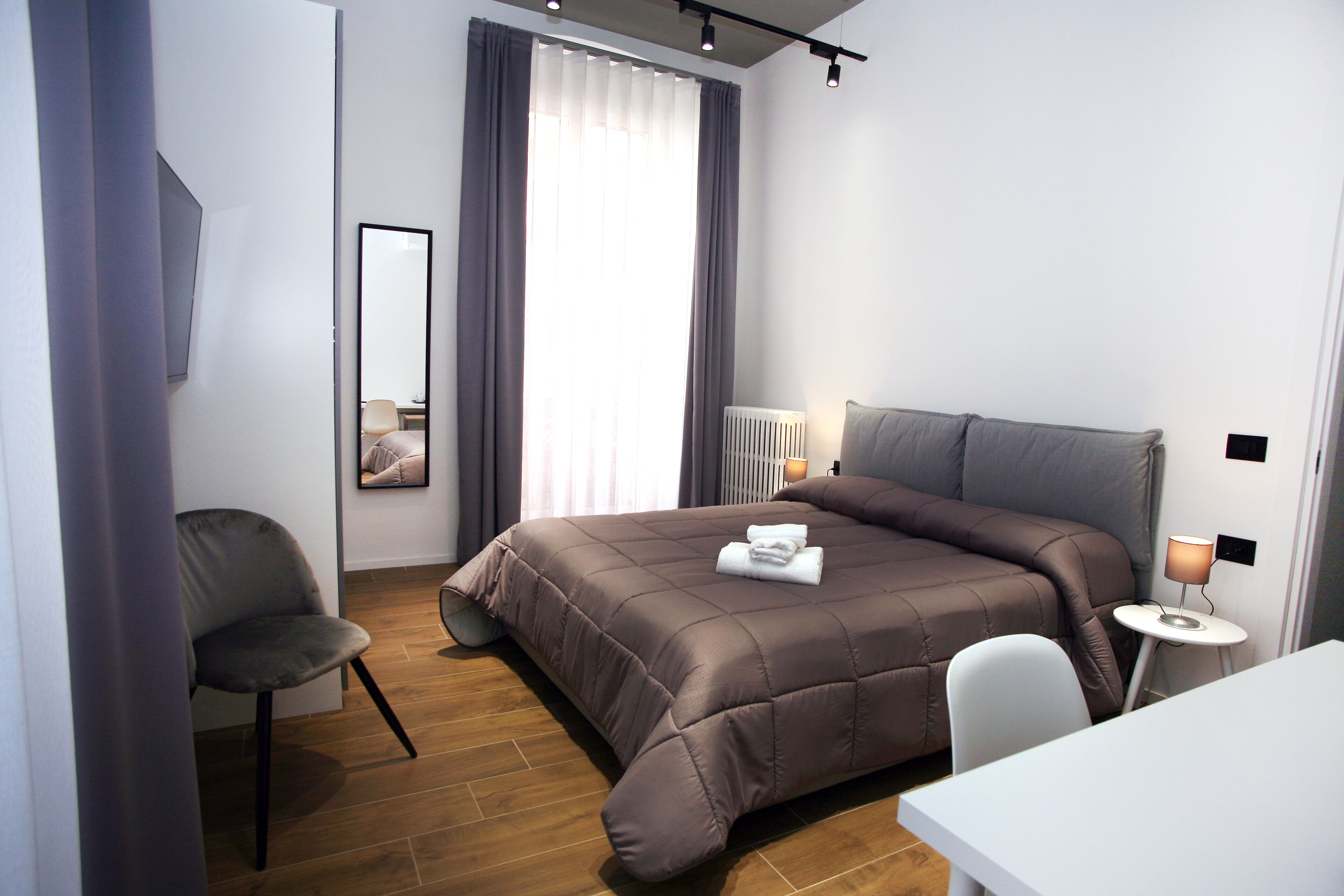 Une chambre d’hôtel moderne avec un grand lit, une table de chevet avec une lampe, une chaise et un miroir.