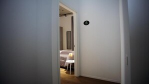A hallway leading to a bedroom with a bed, a nightstand, and a lamp.
