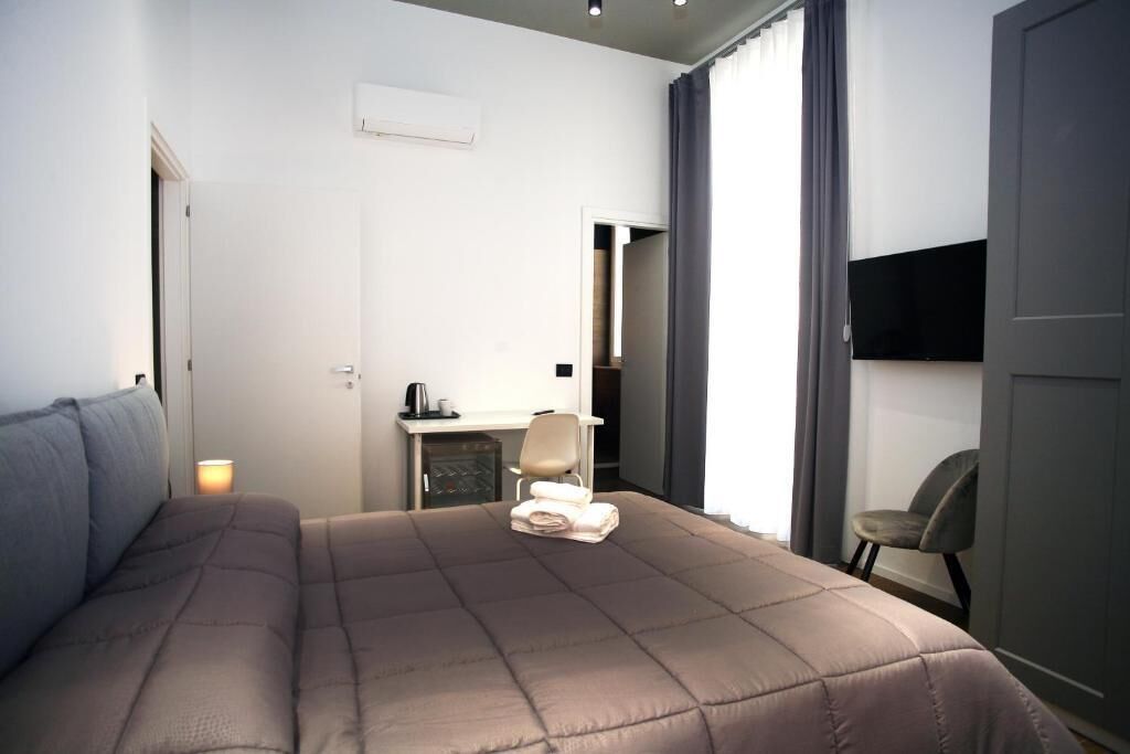 A bedroom with a large bed, a desk with a chair, a TV, and a window with curtains.