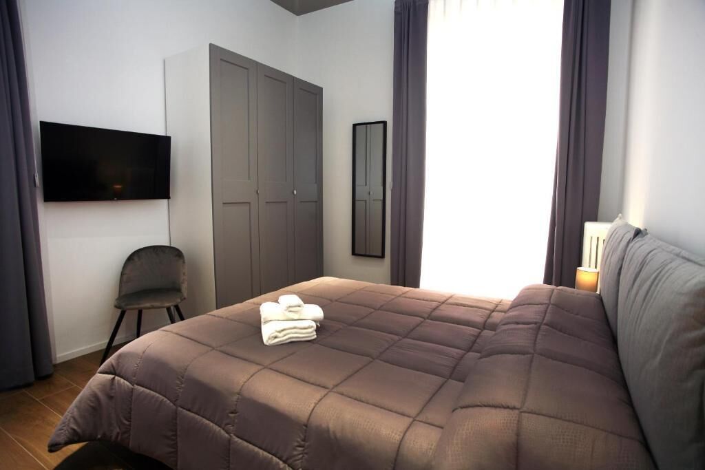A bedroom with a bed, a chair, a wardrobe, a flat-screen TV, and a mirror.