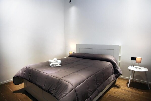 Ein modernes Schlafzimmer mit einem großen Bett, einem Nachttisch mit Lampe und einer Wandleuchte.