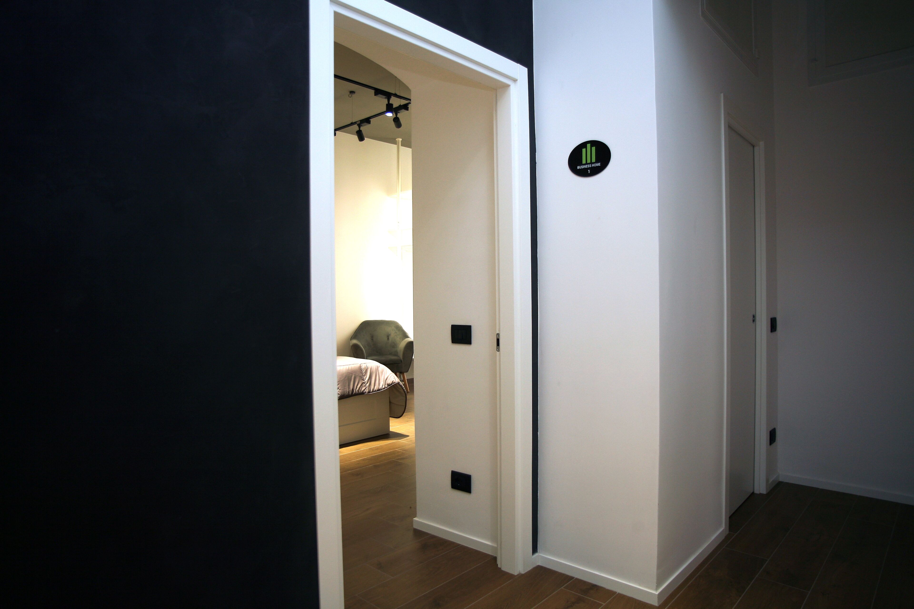 A hallway with a bed in the background, a door with a sign, and a light fixture.