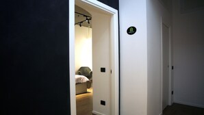 A hallway with a bed in the background, a door with a sign, and a light fixture.