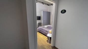 Un couloir étroit mène à une chambre qui contient un lit, une chaise et une petite table.