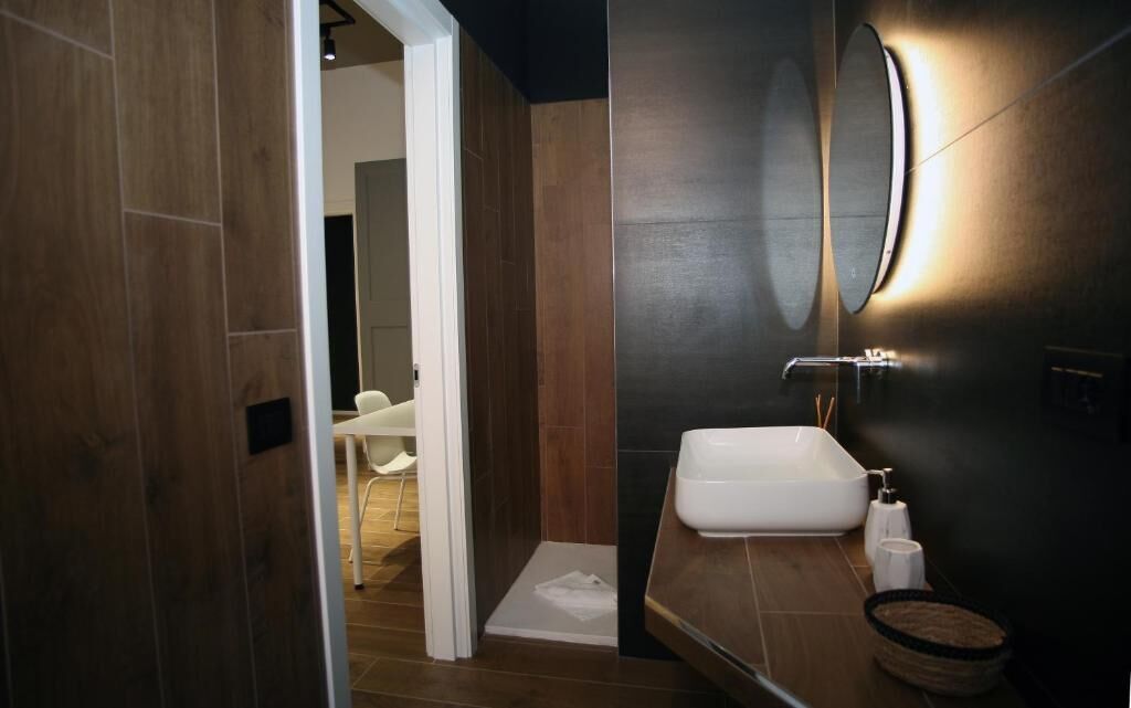 Un baño moderno con un lavabo blanco, un espejo y una zona de ducha.