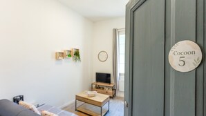 A room with a sofa, a coffee table, a TV, and a door with a sign. - Cozy Studio in Beaucaire Historic Center (Beaucaire)