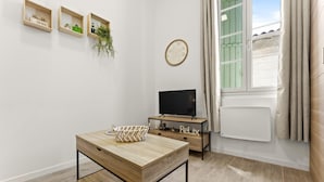 A modern living room with a wooden table, a TV, and a window with curtains. - Cozy Studio in Beaucaire Historic Center (Beaucaire)
