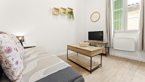 A modern room with a bed, a TV, a wooden table, a small plant, and a window with curtains. - Cozy Studio in Beaucaire Historic Center (Beaucaire)