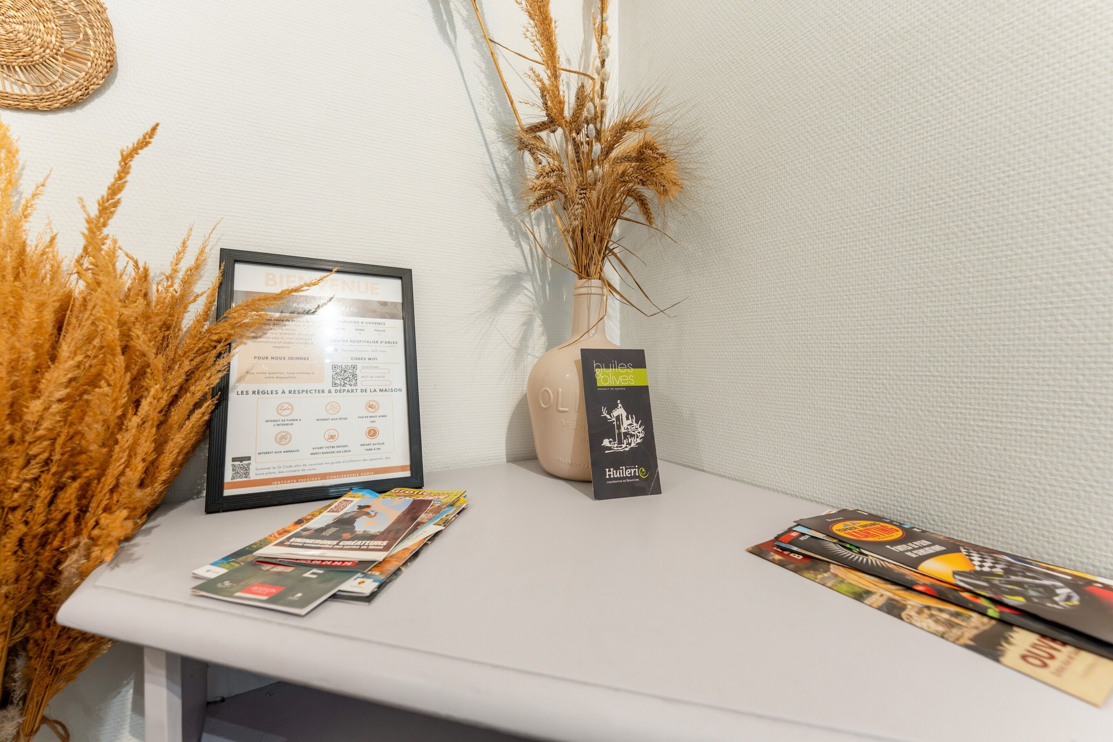 Une table sur laquelle se trouvent un document encadré, un vase contenant des plantes séchées et des brochures.