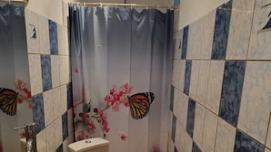 A bathroom with a shower, a toilet, a sink with a mirror, and decorative butterfly and flower tiles. - GROUND-FLOOR HOUSE—GARDEN—ROOMS FOR RENT AND A TERRACE WITH A PING-PONG TABLE (Rivière-Salée)