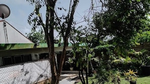 A courtyard with trees, a satellite dish, and a building with a green roof. - GROUND-FLOOR HOUSE—GARDEN—ROOMS FOR RENT AND A TERRACE WITH A PING-PONG TABLE (Rivière-Salée)