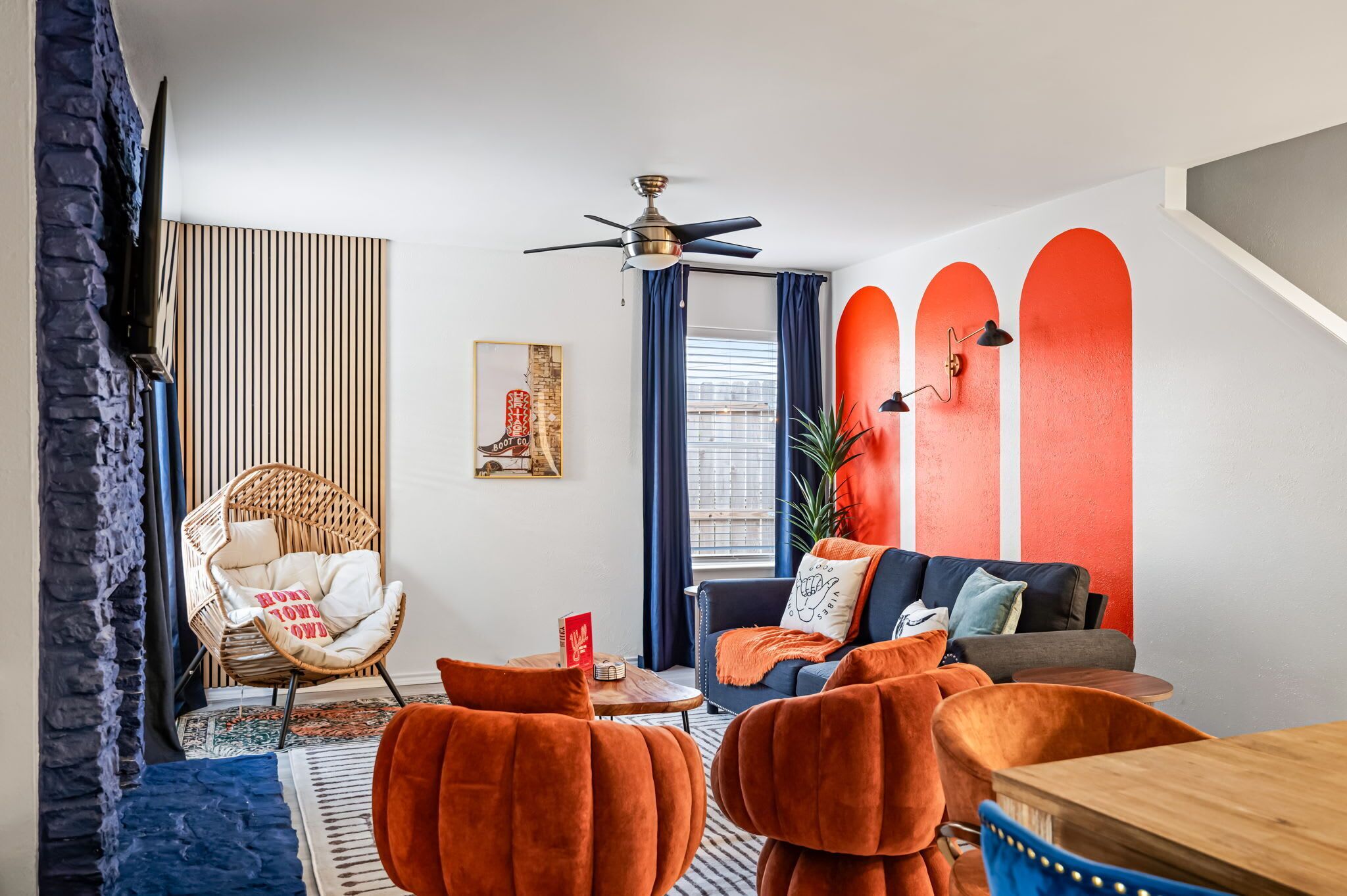 Een moderne woonkamer met een bank, fauteuils, een plafondventilator en een rode accentmuur.