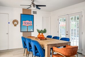 Zona pranzo con tavolo in legno, sedie blu e arancioni, ventilatore a soffitto e insegna con la scritta 'TEXAS'.