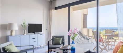 Una sala de estar moderna con sofá, sillón, mesa de centro, televisor y un balcón con mobiliario exterior.