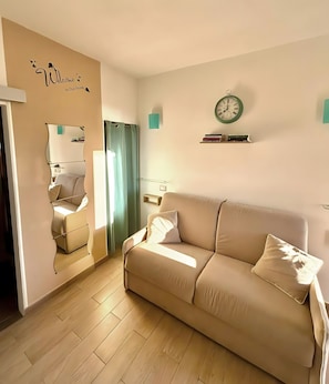 Ein Wohnzimmer mit einem beige farbenen Sofa, einem Spiegel, einer Uhr und einem hellen Holzboden.
