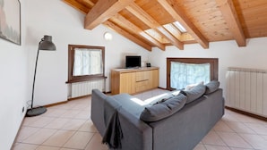 A room with a high wooden ceiling, a sofa, a desk with a computer, and a radiator. - Apartment 'La Mansarda Sul Lago' with Lake View, Wi-Fi and Air Conditioning (Lovere)