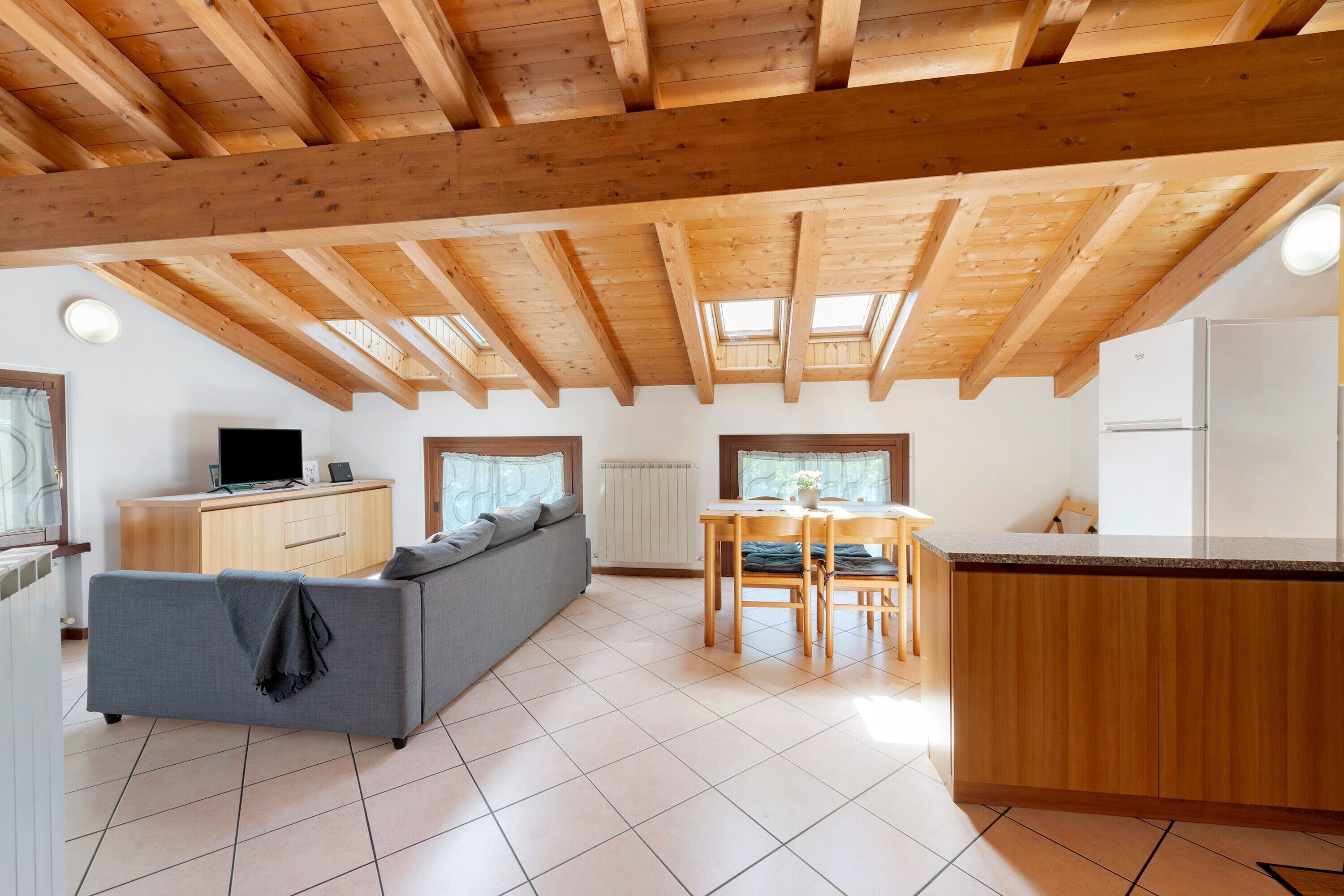 Ein modernes Interieur mit Holzbalkendecke, einer Couch, einem Esstisch und einer Küchenzeile.