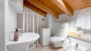 A bathroom with a sink, toilet, and bidet, wooden ceiling beams, and tiled walls. - Apartment 'La Mansarda Sul Lago' with Lake View, Wi-Fi and Air Conditioning (Lovere)