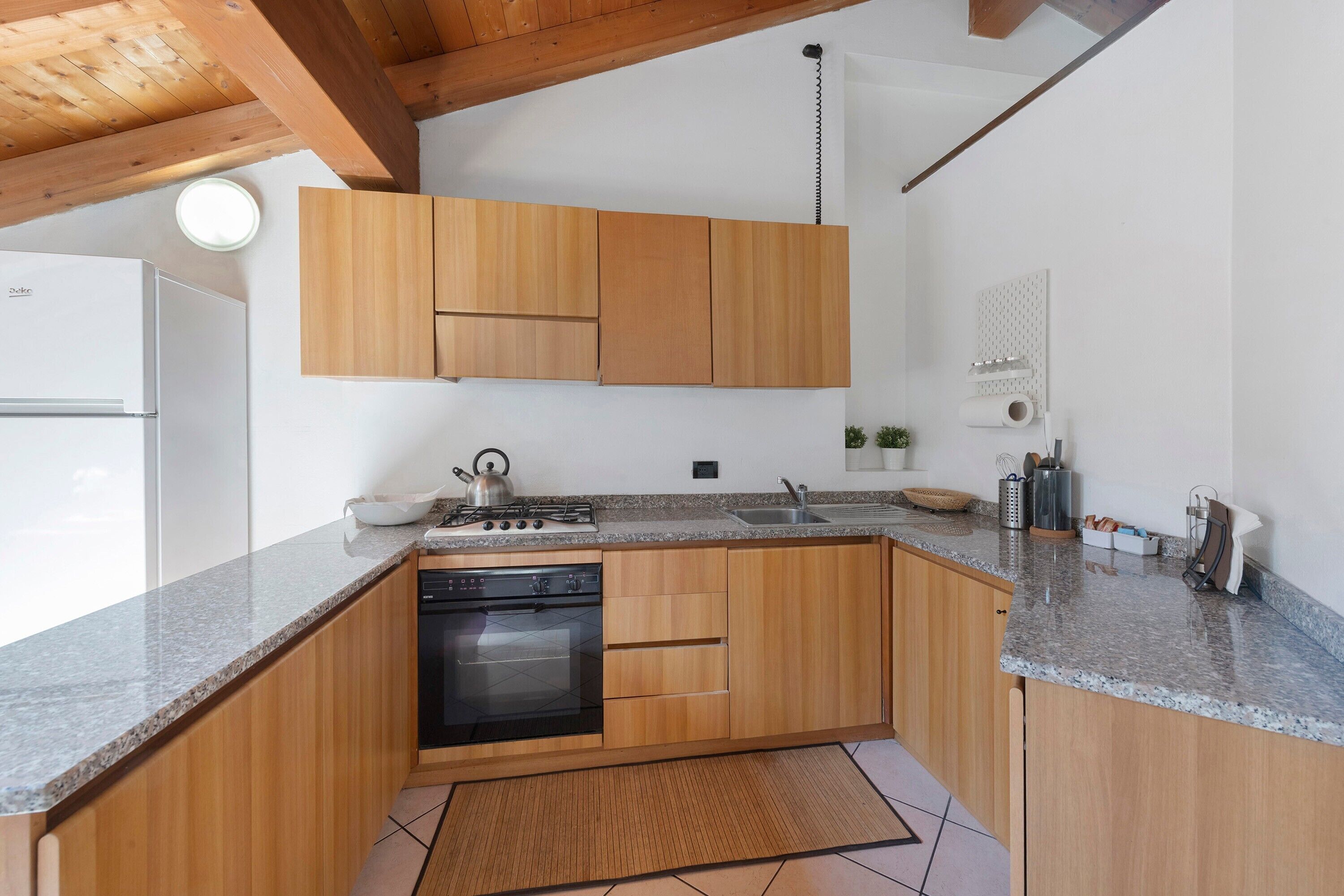 Eine Küche mit Holzausstattung, integriertem Backofen, einer Granit Arbeitsplatte und einer kleinen Kochinsel mit Wasserkocher.