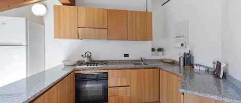 A kitchen with wooden cabinets, a built-in oven, a granite countertop, and a small island with a kettle.