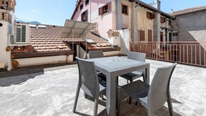 A rooftop terrace with a table and chairs, a metal railing, and a building with a tiled roof and balconies. - Apartment 'La Mansarda Sul Lago' with Lake View, Wi-Fi and Air Conditioning (Lovere)