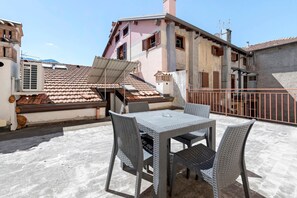 Una terrazza sul tetto con tavolo e sedie, una ringhiera in metallo e un edificio con tetto in tegole e balconi.