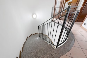 A spiral staircase with a metal railing, a round landing, and a light fixture on the wall.