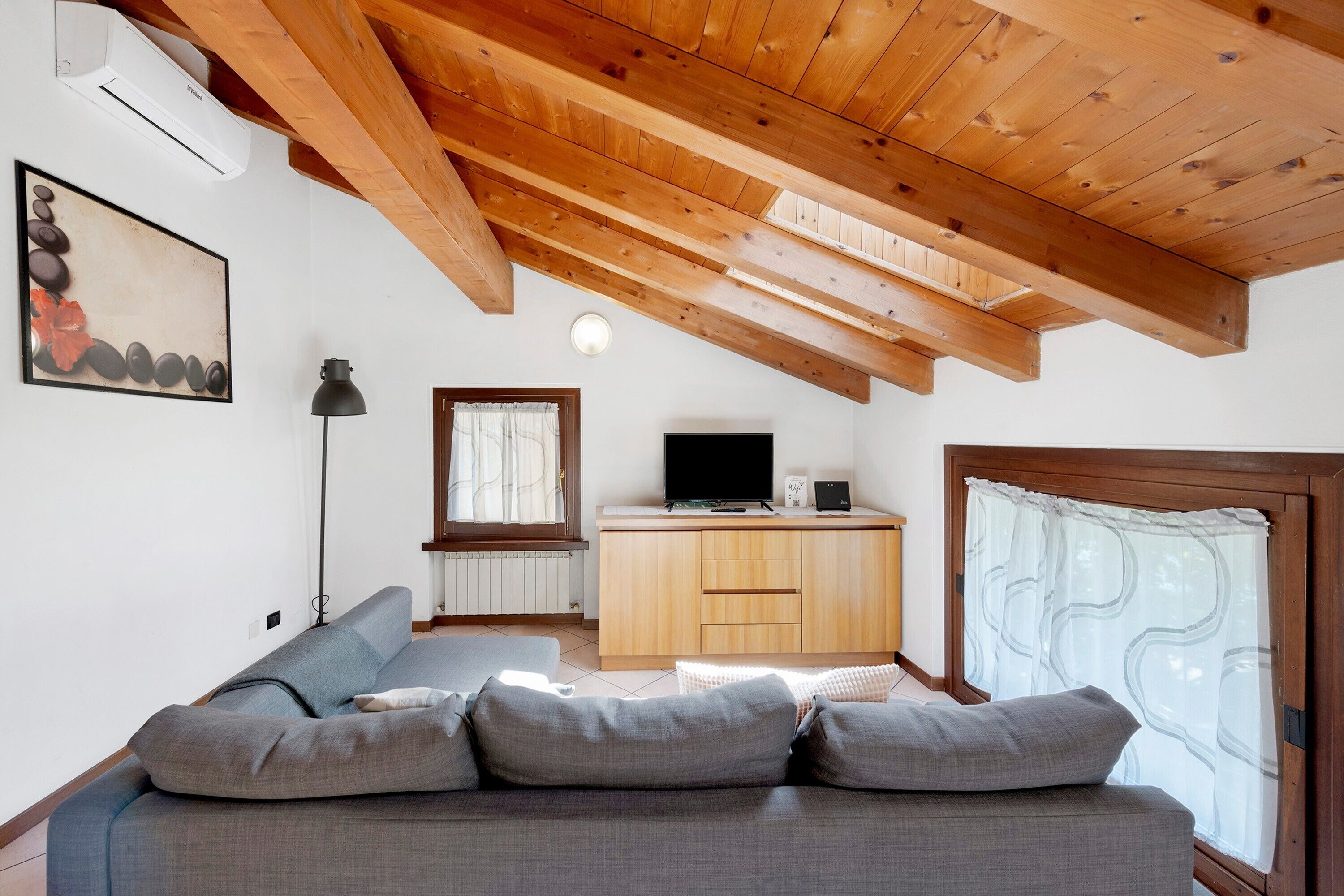 A modern living room with a wooden ceiling, a sofa, a television, and a window with curtains.