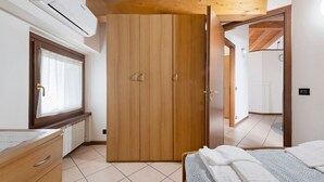 A bedroom with a wooden wardrobe, a bed with white linens, a window with curtains, and a tiled floor. - Apartment 'La Mansarda Sul Lago' with Lake View, Wi-Fi and Air Conditioning (Lovere)