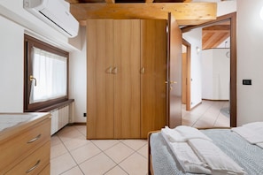 Una camera da letto con un armadio in legno, un letto con lenzuola bianche, una finestra con tende e un pavimento piastrellato.