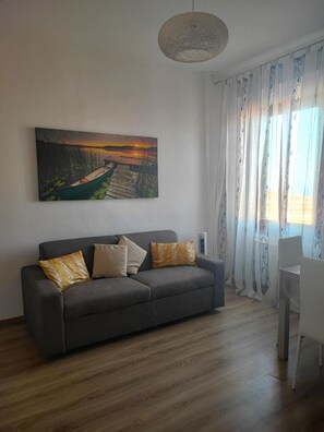 Un soggiorno moderno con un divano grigio, un quadro raffigurante un tramonto e una poltrona bianca.
