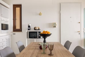 A dining area with a wooden table, two chairs, a bowl of fruit, and a television on a stand. - Il Sole di Giada | Sea View by Mondello Bay (Palermo)