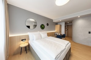 Moderni hotellihuone, jossa on suuri sänky, yöpöytä ja pyöreä peili.