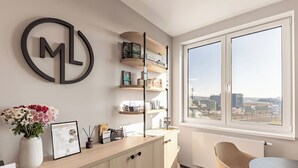 A modern office space with a desk, shelves, a vase with flowers, a framed certificate, and a large window with a city view.