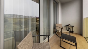 A balcony with a view of buildings, a chair, a small table, and a sofa.
