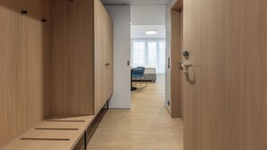 A corridor with wooden lockers, a bed, and a chair in a room with a light-colored floor and walls.