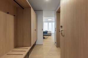 A corridor with wooden lockers, a bed, and a chair in a room with a light-colored floor and walls.
