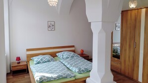 Quarto com cama de madeira, duas mesas de cabeceira, abajur vermelho, espelho e guarda-roupa.