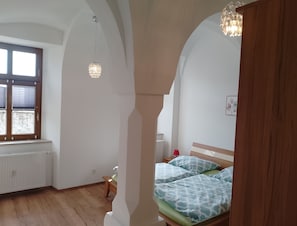 A bedroom with a wooden bed, a radiator, a window with blinds, and a hanging light fixture.