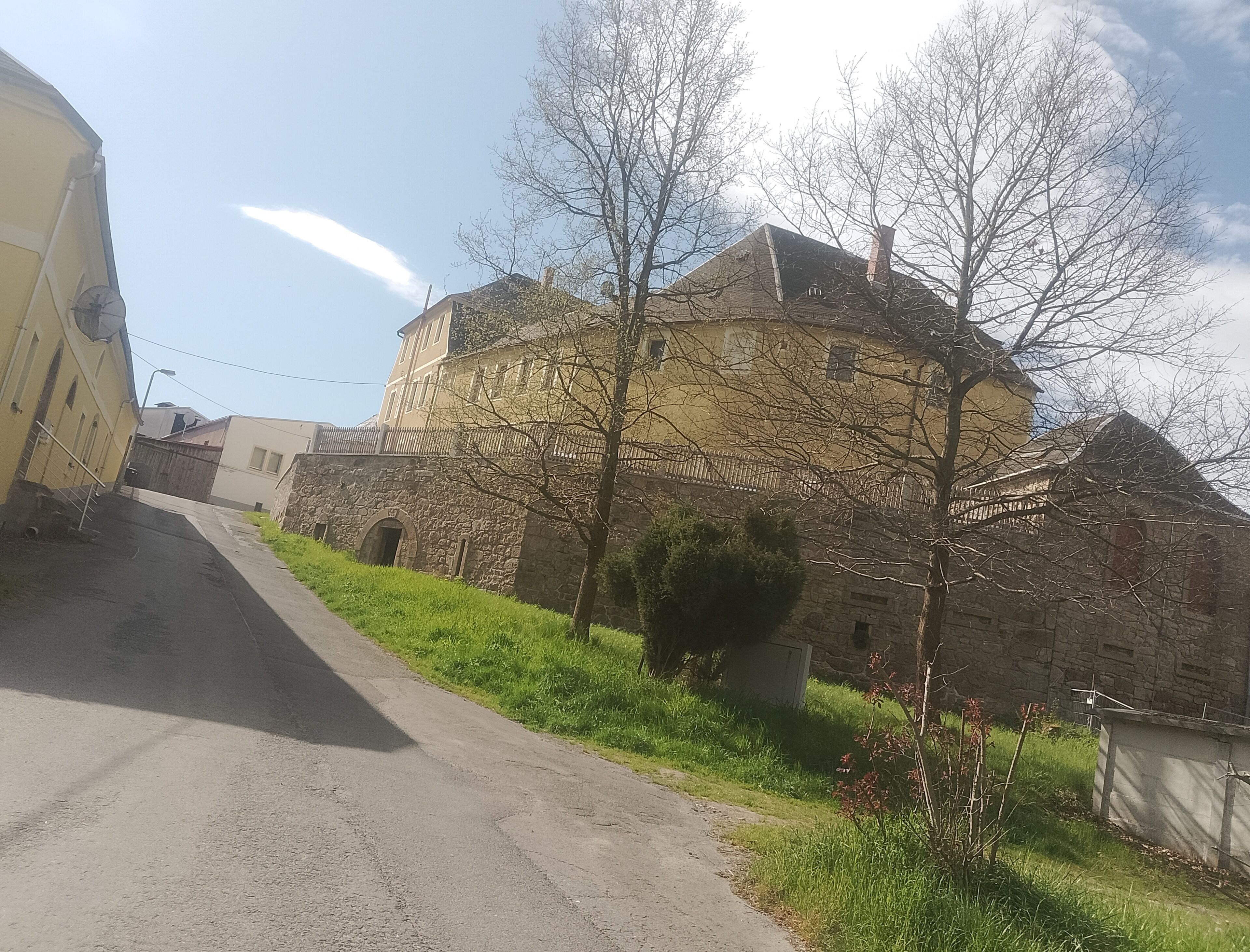 Ein historisches Gebäude mit einer Stein-Fassade und einem zentralen Turm, eine gepflasterte Straße führt dorthin.