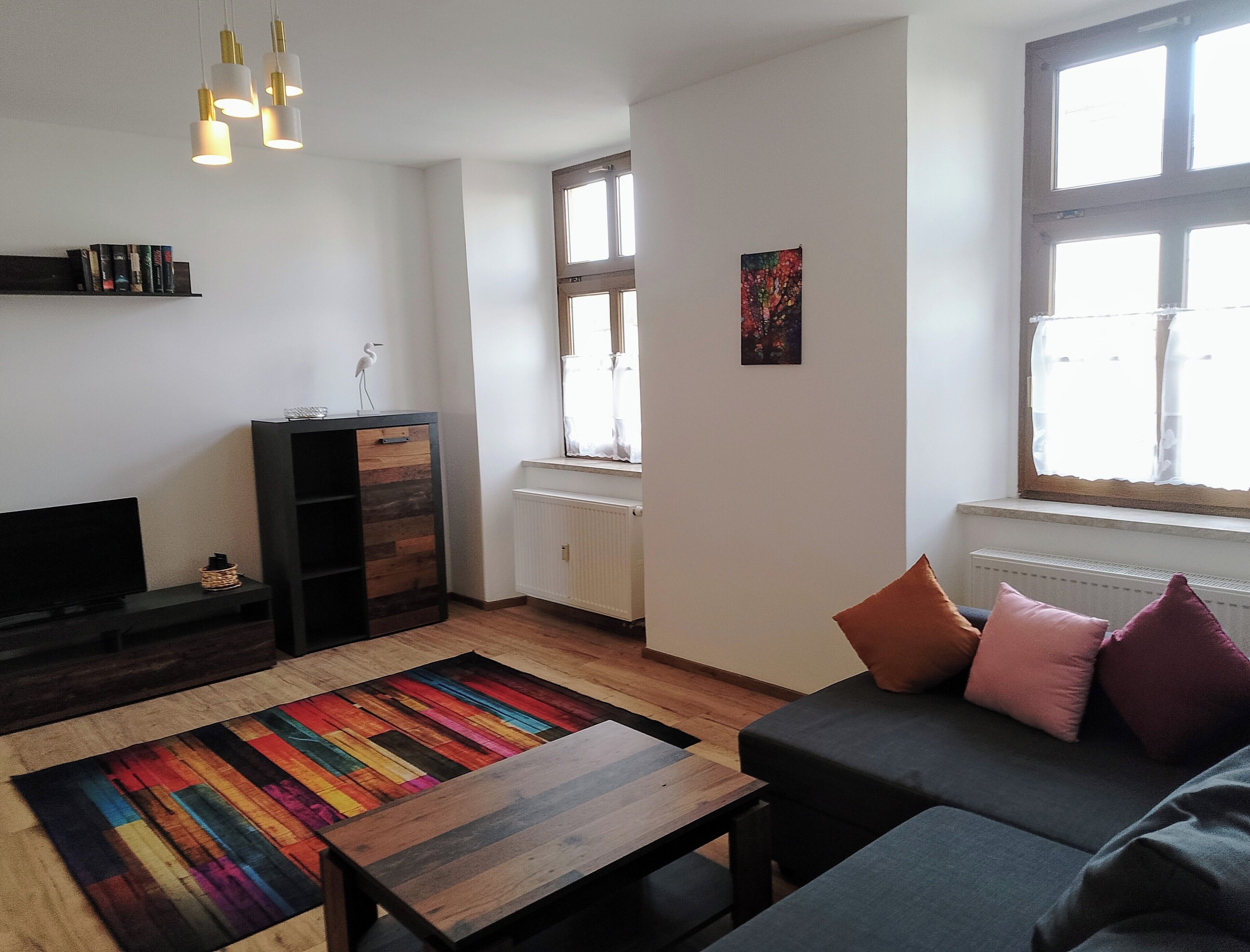 Un salon moderne comprenant un canapé, une table basse, un téléviseur, une bibliothèque et une fenêtre avec des rideaux.