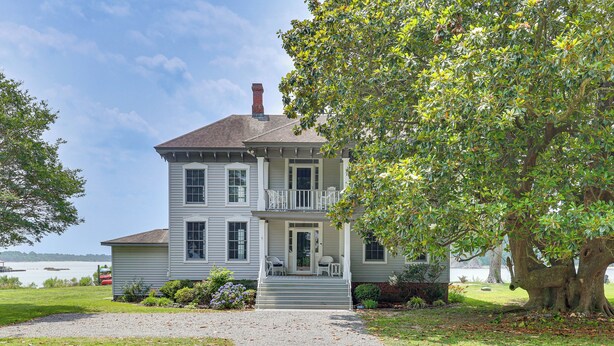 Une maison à deux étages avec un porche à l’avant, une cheminée et un grand arbre au premier plan.