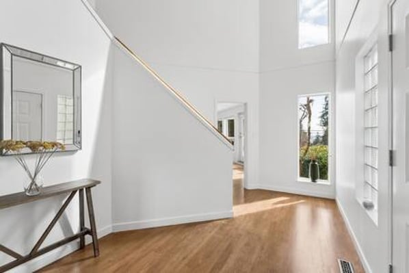Ein Flur mit Holzboden, weißen Wänden, einem Spiegel und einer Treppe, die in einen anderen Raum führt.